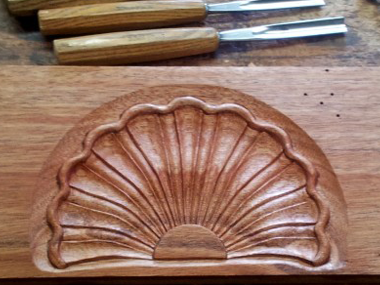 A scalloped shell is carved into a piece of wood in this woodworking class.